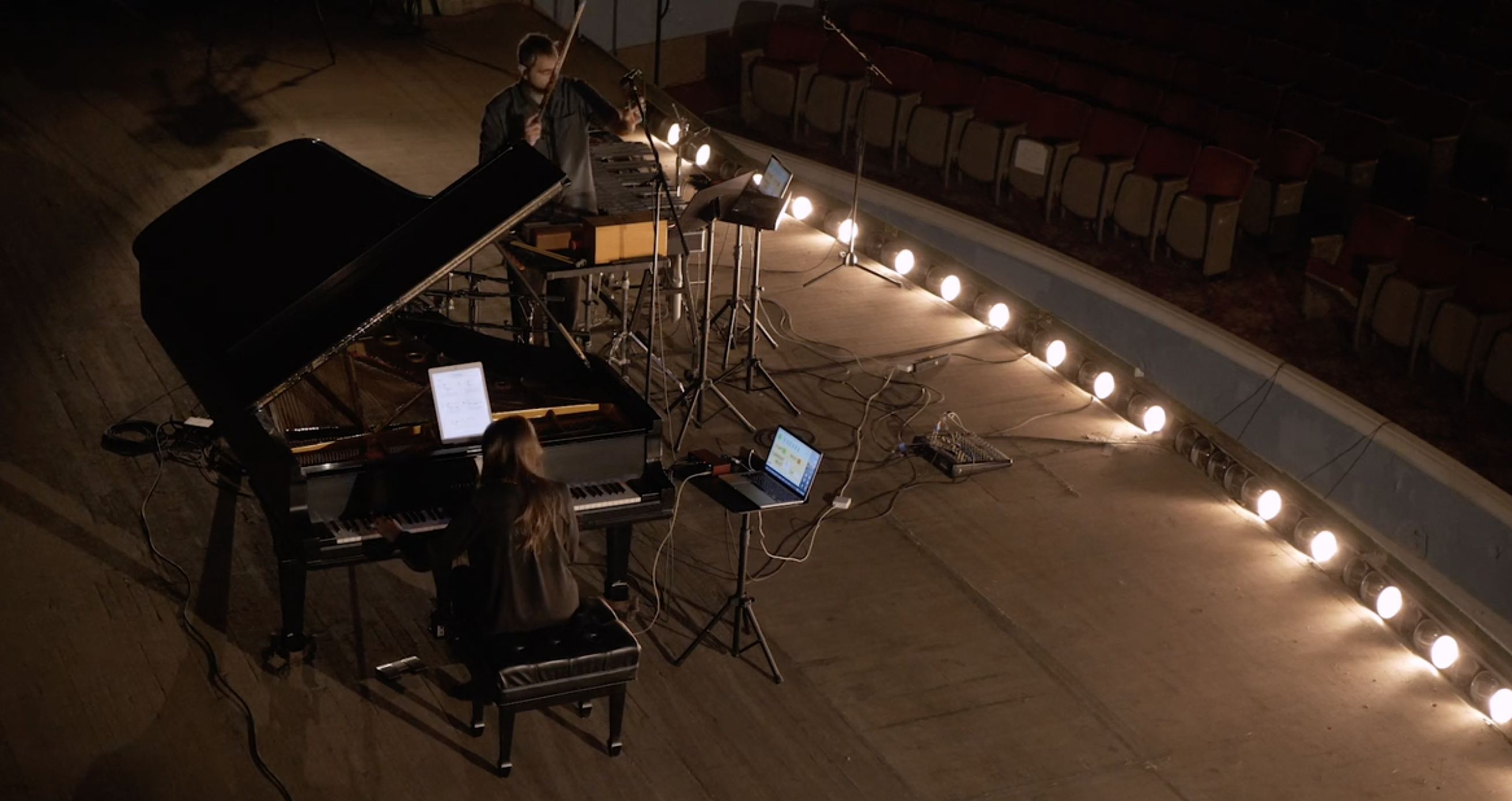 view from above of pianist at a grand piano and percussion setup with stage lights shining upward from the right side