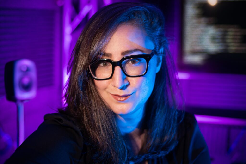 headshot of Tina in a studio with a monitor in the background with code on it; the background is purple